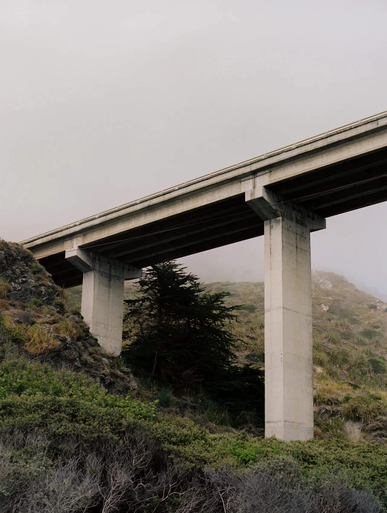 An image shot from below of a tall bridge with a gray sky above it