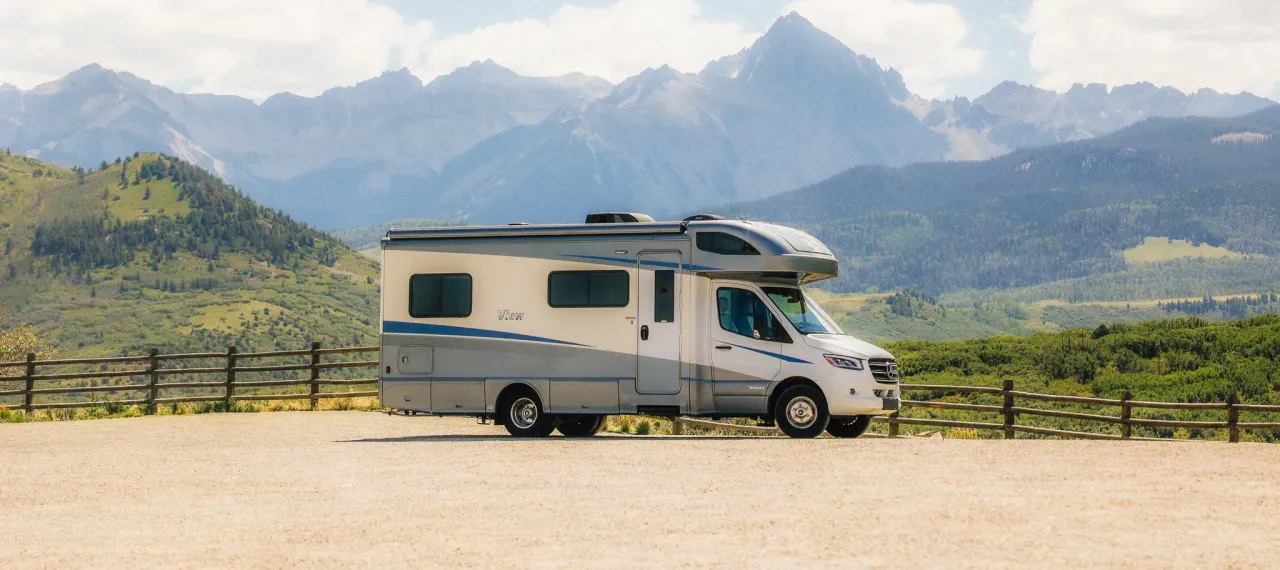An RV is parked in front of tall snow-capped mountains.